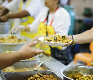 Volunteers serving hot food onto a plate at Feed My Sheep