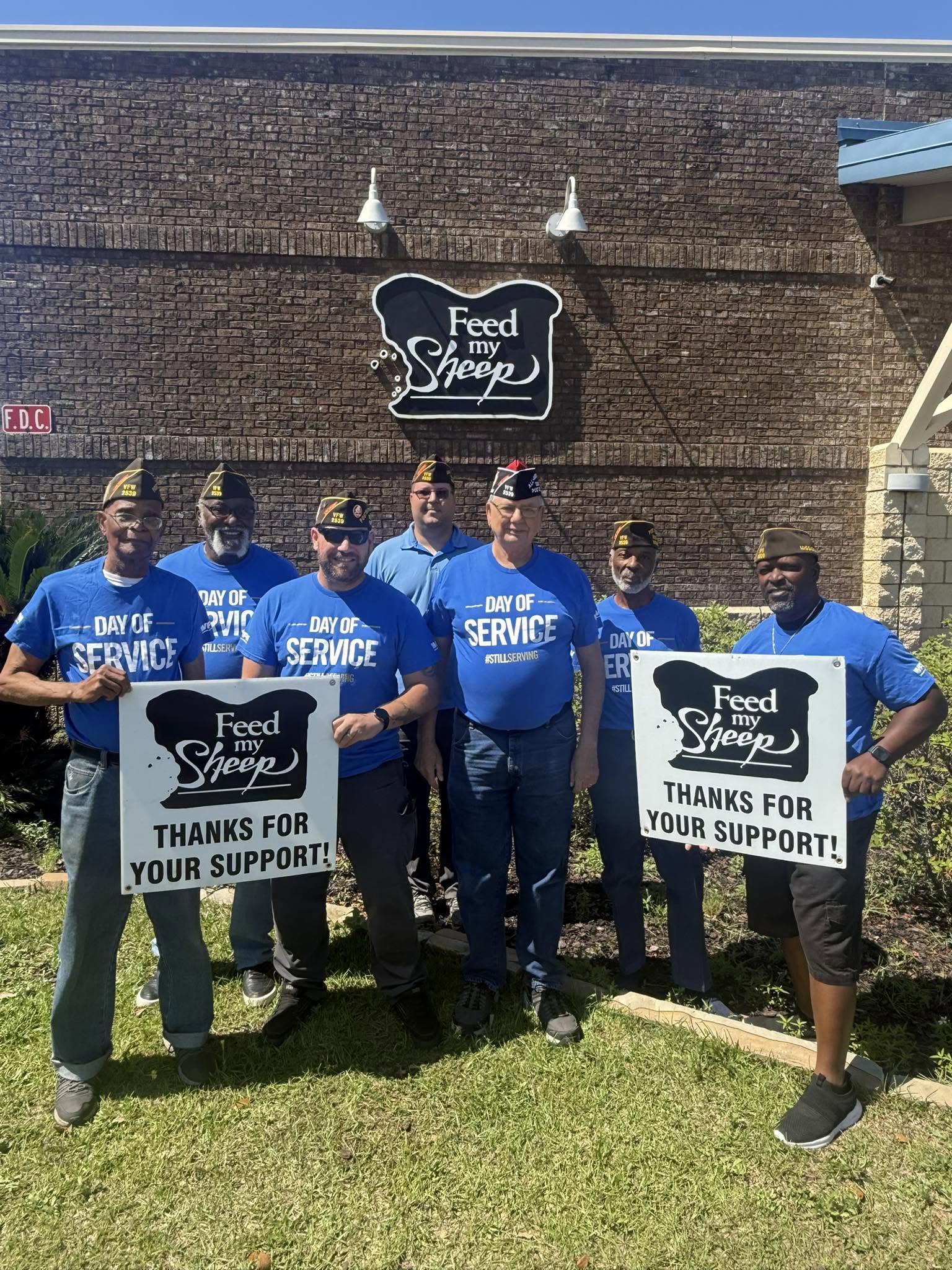 Volunteers from a Day of Service holding 'Thanks for your support' signs outside Feed My Sheep